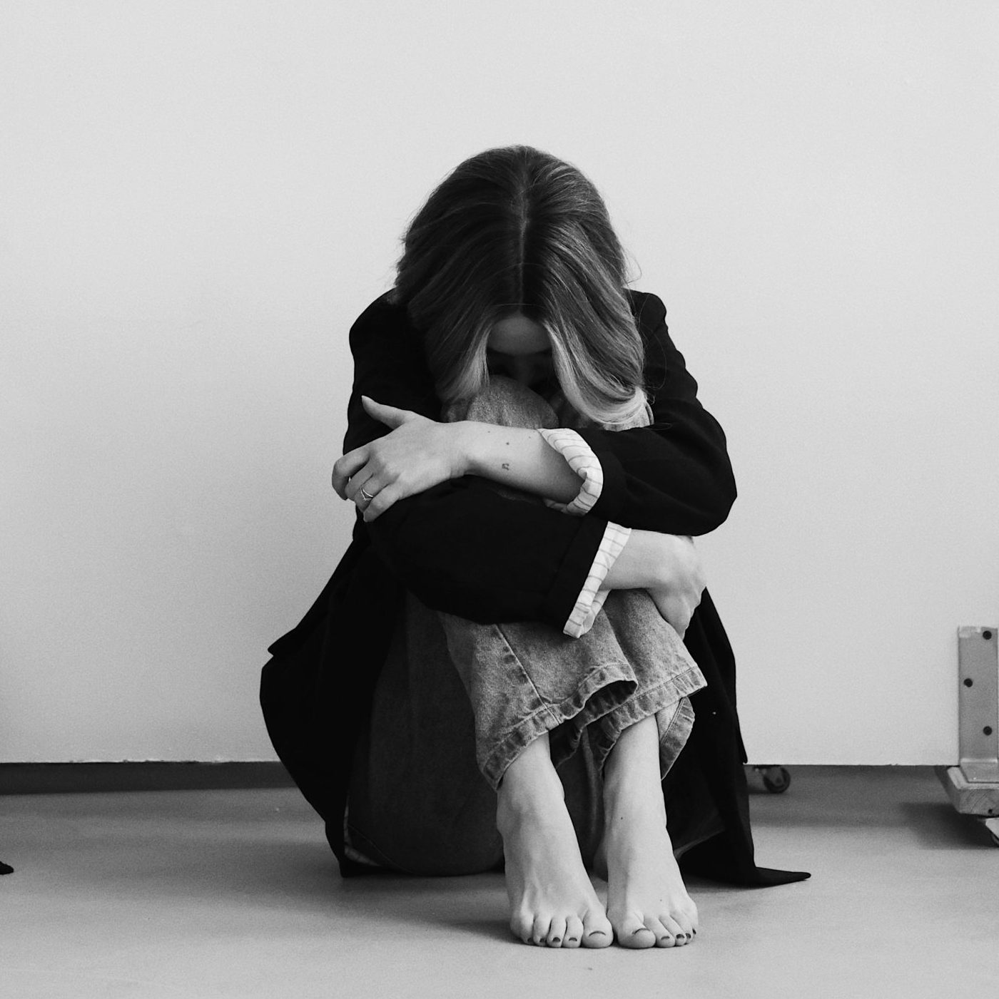 woman in black and white, hugging her legs with her head down between her knees.