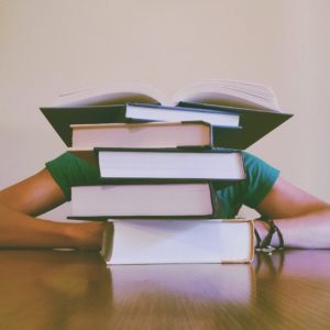 Some poor person, barely visible behind a large stack of books.